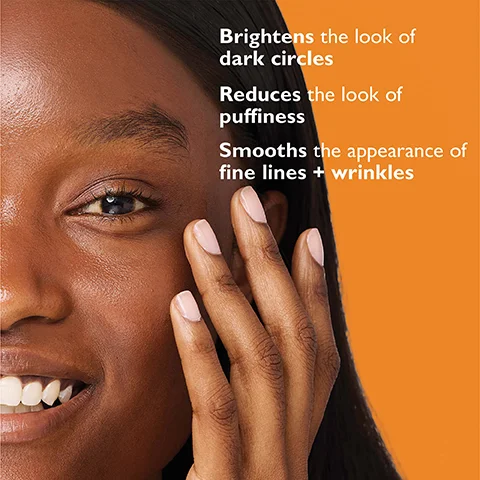 A close-up of a persons face and hand on an orange background with text reading Brightens the look of dark circles Reduces the look of puffiness Smooths the appearance of fine lines + wrinkles.
