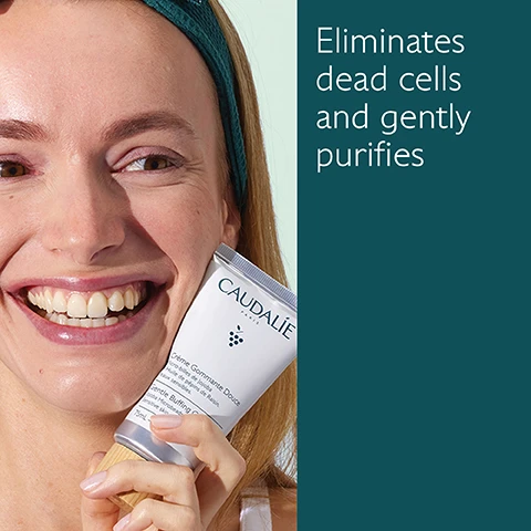 Image 1 - A smiling woman holds a tube of Caudalie skin product close to her face, with text beside her that reads eliminates dead cells and gently purifies.
Image 2 - A tube of Caudalie Gentle Buffing Cream is placed on a textured surface, surrounded by a green grape and highlighting ingredients: Jojoba microbeads for cleansing and exfoliating, Grapeseed oil for nourishment, and Honey for softening, with the tube labeled Crème Gommante Douce and showing the volume as 75 mL.
Image 3 - Image shows two skincare products from Caudalie: a light green tube labeled Deep Cleansing Exfoliator with the text Deeply purifies, Volcanic sand microbeads, All skin types and a dark green tube labeled Buffing Cream with the text Gently purifies, Jojoba microbeads, Sensitive skin.
Image 4 - A hand is holding a tube of Caudalie skincare product while squeezing out a small amount onto the palm of another hand, with the text Apply to damp skin 1-2 times a week visible.