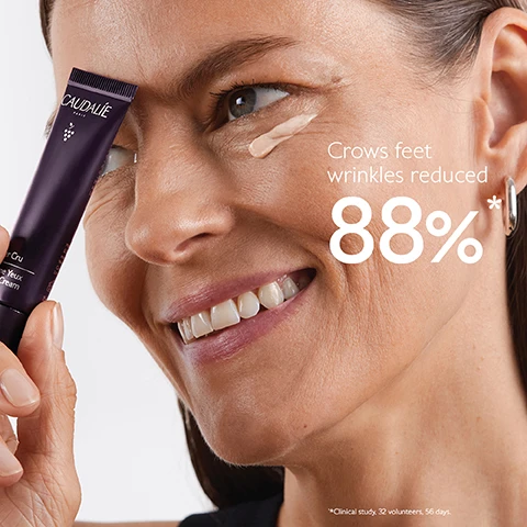 Image 1 - A woman is smiling and applying a cream under her eye, holding a tube labeled Caudalie Premier Cru Eye Cream, with text stating Crows feet wrinkles reduced 88%* below.
Image 2 - A tube of Caudalie Premier Cru eye cream is placed against a purple background, surrounded by clusters of dark grapes, with text highlighting its features: Natural plumping filler improves skin volume, Longevity patent stimulates youth proteins, and Blend of pearlizers instantly illuminates.
Image 3 - A woman with long brown hair smiles while holding a bunch of dark grapes in one hand and a grape in the other, with text on the left side reading Targets all signs of ageing followed by three checkmarks for Wrinkles, Dark circles, and Puffiness.
Image 4 - A hand holds a small, dark tube of eye cream with a silver applicator tip, accompanied by instructions on how to recycle it, stating to separate the applicator from the tube and recycle the tube with Terracycle.
Image 5 - A person applying a cream under their eye with a silver applicator while showing a smooth skin texture, with the text 84% saw a smoother and brighter-looking eye contour* underneath.
Image 6 - Image shows three eye cream tubes from Caudalie against a purple background, labeled Premier Cru for all signs of ageing, Resveratrol-Lift for anti-puffiness and eyelid-firming, and Vinoperfect for all types of dark circles, with the question Which eye cream suits your skin? displayed above.
Image 7 - Image shows four swatches of skincare products on a purple background labeled The Premier Cru Routine, with the products named as follows from top to bottom: The Serum, The Cream, The Rich Cream, and The Eye Cream.
Image 8 - A purple tube of Caudalie Premier Cru The Eye Cream is shown against a split background, with text stating New, Premier Cru The Eye Cream, New longevity formula, and New natural plumping filler from rosewood.