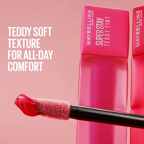 Image 2 - A fuzzy applicator wand with red lip product on its tip is shown against a pink background, with two pink lip tint tubes in the background, one prominently displaying Maybelline New York Super Stay Teddy Tint and the other Maybelline New York, alongside the text Teddy Soft Texture For All-Day Comfort. Image 3 - A fluffy pink bear-like figure stands against a split background, with a light pink side featuring floating cubes on the left and a dark red side with swirling white powder on the right, displaying the text TINTED TECHNOLOGY, BOUNCY POLYMERS, and BLURRING POWDERS. Image 4 - A blonde woman wearing pink eyeshadow and matte pink lipstick holds two Maybelline Super Stay Teddy Tint lipsticks near her chin against a blurred cityscape, with accompanying text reading BLURRED MATTE, UP TO 12H WEAR, NO TRANSFER, and the lipstick packaging states MAYBELLINE NEW YORK, SUPER STAY TEDDY TINT. Image 7 - Eight teddy bear-shaped makeup swatches in various shades are shown on a pink background, with the text 8 TEDDY-SOFT SHADES Current Mood Skinny Dip Mascara Tear Baby Tee Coquettish July Forever Wild At Heart Petalcore.