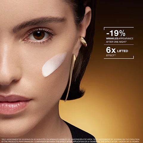 A close-up of a womans face features a white cream applied in a streak on her right cheek, with a distinctive gold earring visible against a dark brown to golden gradient background, displaying text that reads -19% WRINKLES APPEARANCE AFTER ONE NIGHT* and 6X LIFTED EFFECT**, followed by a smaller disclaimer text *SELF-ASSESSMENT BY SCORING ON 32 SUBJECTS, ON WRINKLES VISIBILITY OF UNDERNEATH EYE AREA **SELF-ASSESSMENT BY SCORING ON THE EVOLUTION OF THE PRODUCTS PERFORMANCES. COMPARISON BETWEEN THE EFFECT AFTER APPLICATION ON 34 WOMEN VS. THE EFFECT AFTER 1 MONTH ON 33 WOMEN.